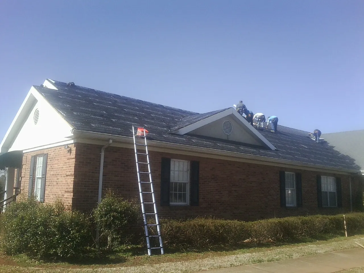 Crew tearing shingles off a brick ranch roof with a ladder set — Metal Roof Repair work by our crew in Haltom City