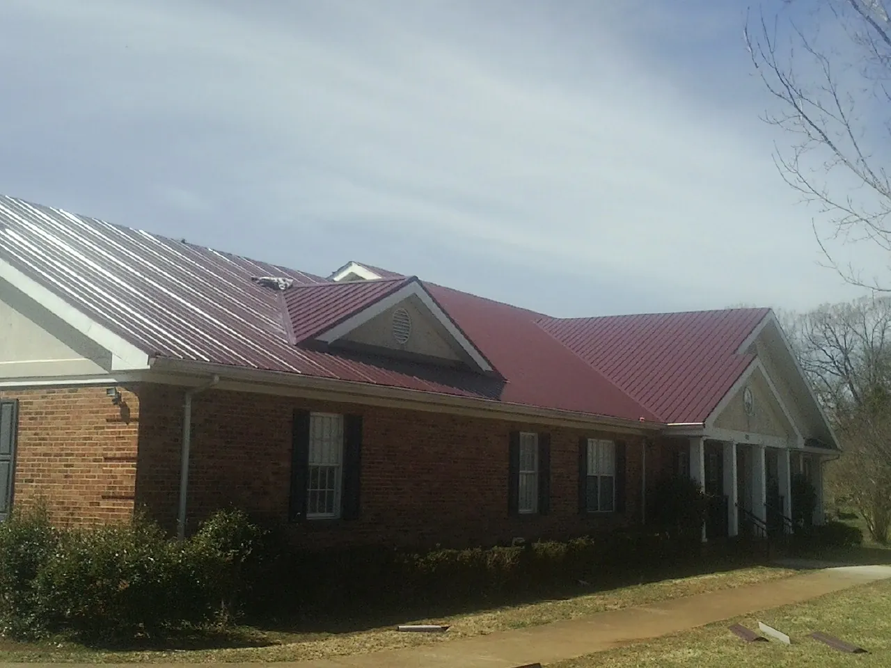 Red metal roof with gabled entries on a long brick building, from a Hail Damage Roof Repair job in Haltom City