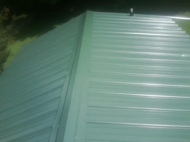 New green metal panels meeting at the ridge of a roof — Flat Roof Repair work by our crew in Haltom City