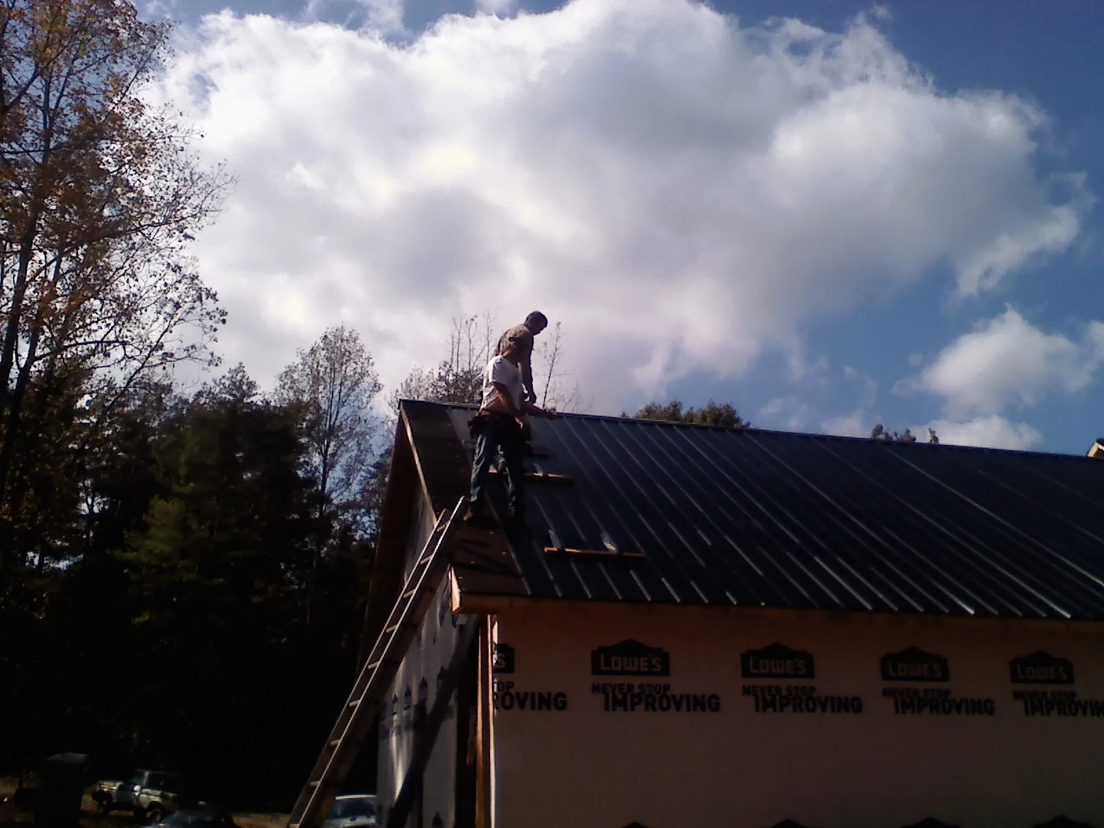 Roofer fastening dark metal panels high against a cloudy sky, from a Roof Inspection job in Haltom City