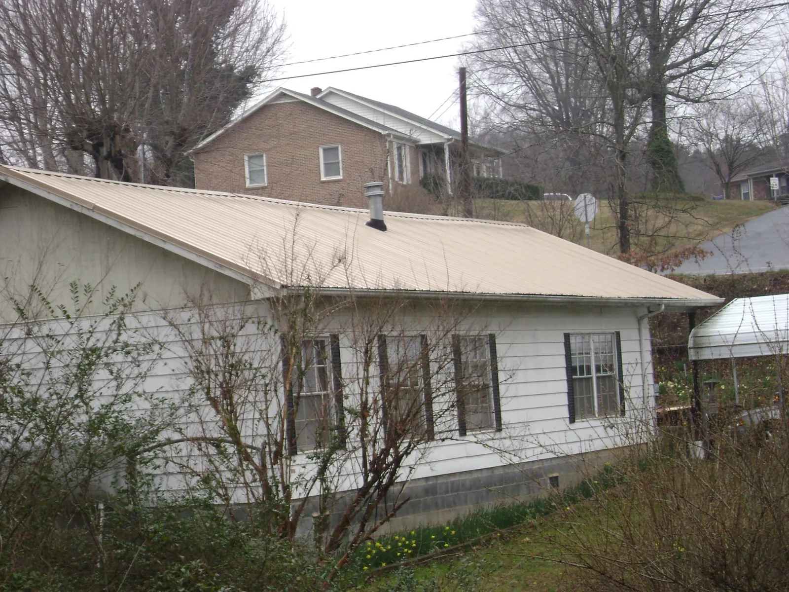 Tan metal roof on a white sided house set into a hillside — Commercial Roofing by Roofing Brothers in Haltom City