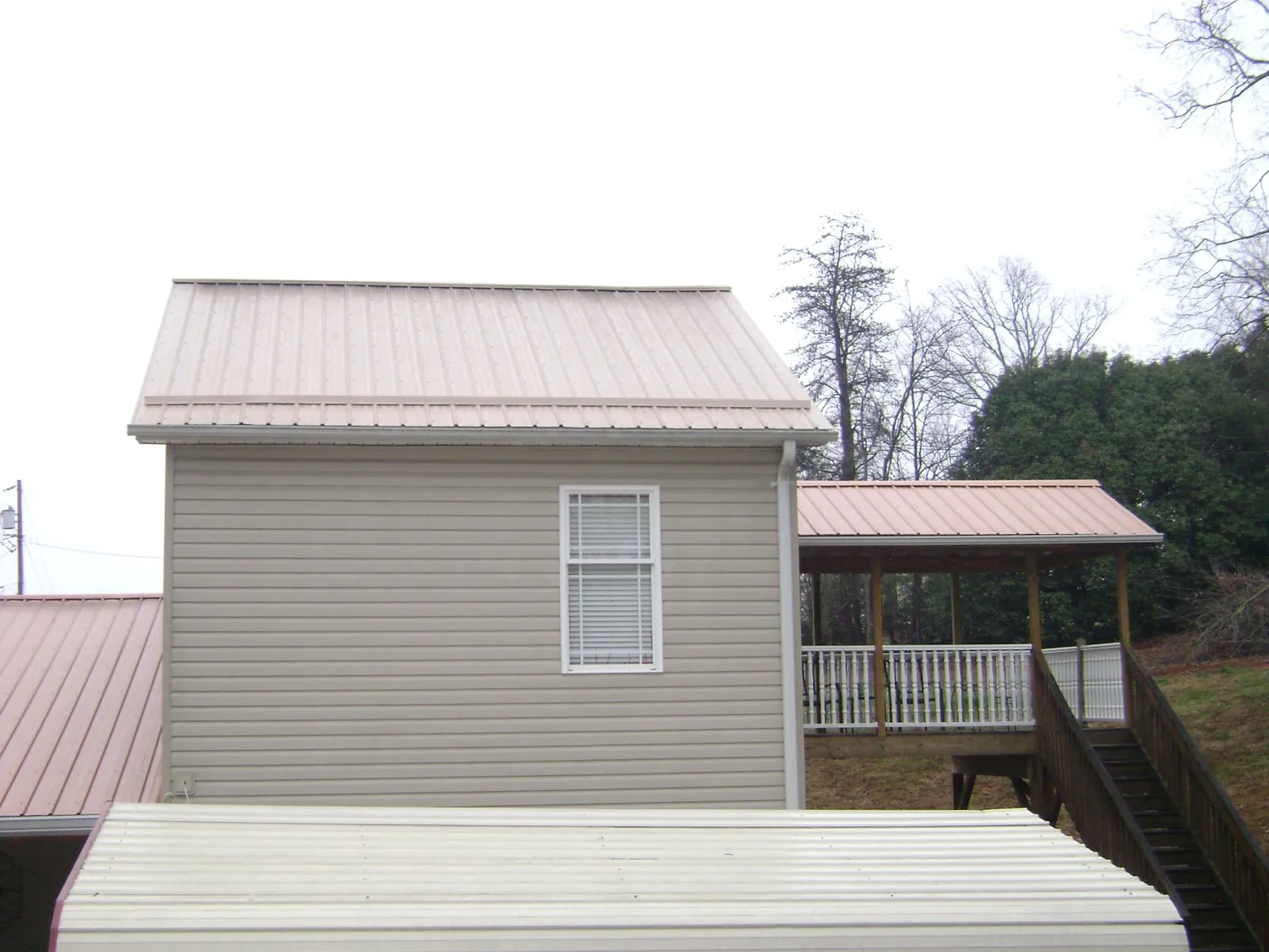 Tan metal roofs on a two story addition and attached porch, from a Roof Replacement job in Haltom City